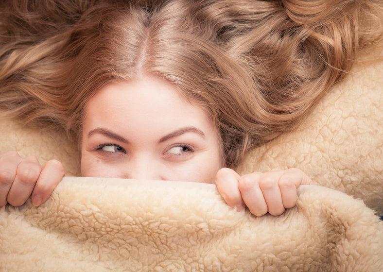 a women smiling through blanket after achieving beauty sleep