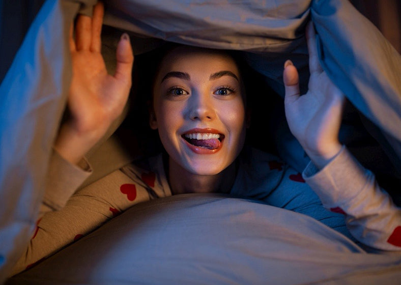 a happy teenage girl lying under a blanket in bed
