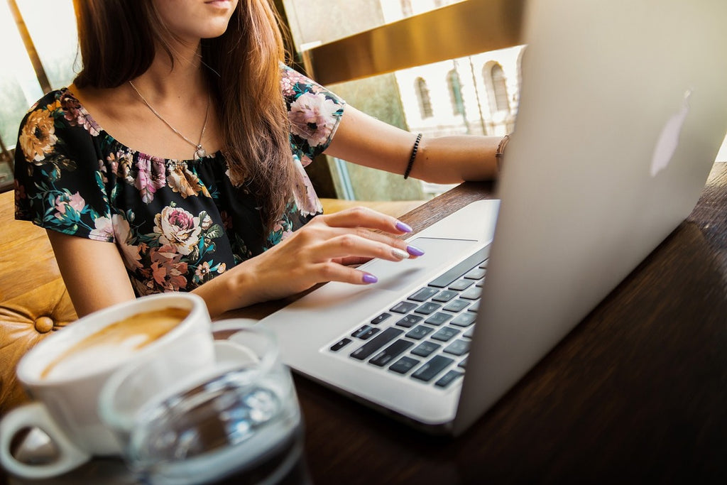 Woman sat at a laptop in a cafe, shopping online for second-hand clothes