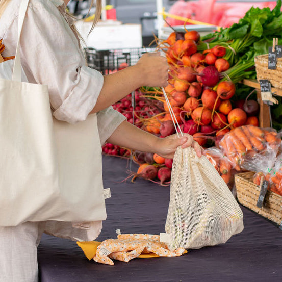 A person uses Market Bags reusable cloth produce bags to secure her famers market veggies.