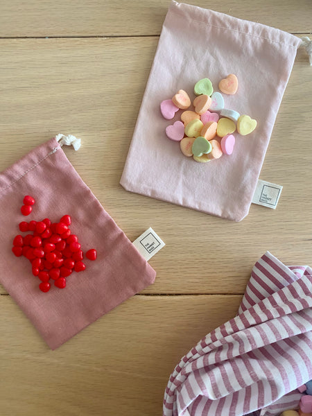 Small cloth reusable bags with cinnamon hearts and conversation hearts laying on top of them