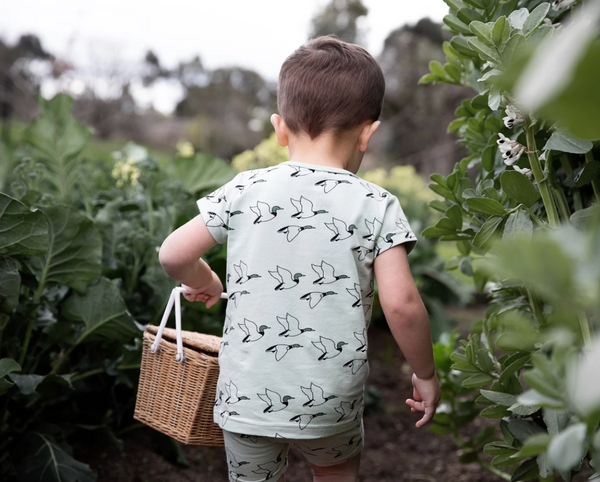 A boy in the bushes holding a basket and wearing The Rest clothing.