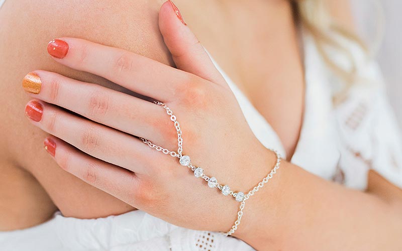 Alek crystal hand chain bracelet on left hand touching right shoulder wearing white dress