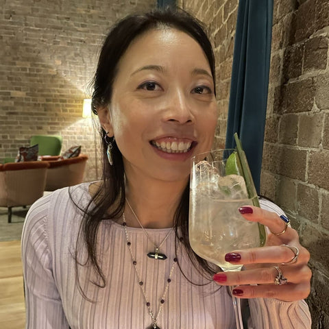 Cynthia Lau at a bar next to a grey brick wall with a drink