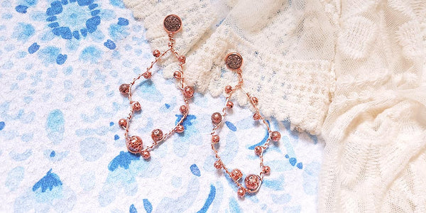 Pair of rose gold lava rock earrings flatlay on blue towel and white dress
