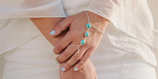 Close up left hand holding right wrist wearing Skye turquoise hand chain with turquoise nails and white dress