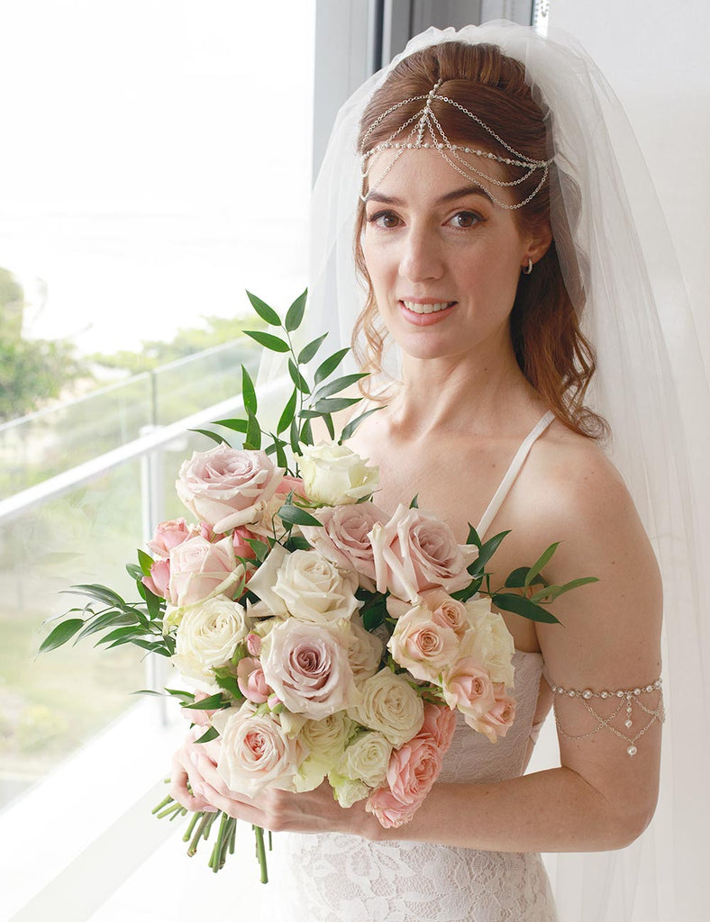 Bride Frances on balcony wearing custom made head chain with veil and arm bracelet holding a flower bouquet