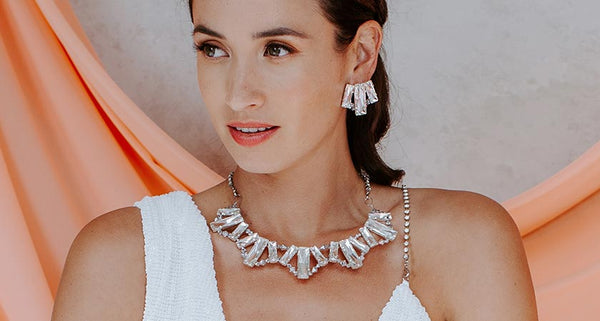 Lucia wearing Kara crystal statement necklace and matching Kara crystal earrings in a white dress