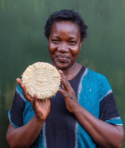 Woman artisan from Africa holding a raffia coaster she made by hand