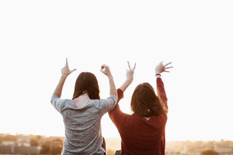 Two women sitting beside each other with their backs to the camera spelling love with their fingers.