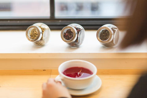 Tea cup full of tea with glass loose leaf tea containers in background.