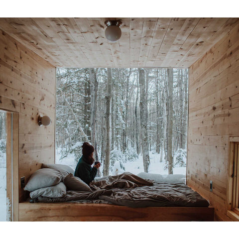 A woman drinking from a mug in bed in winter.