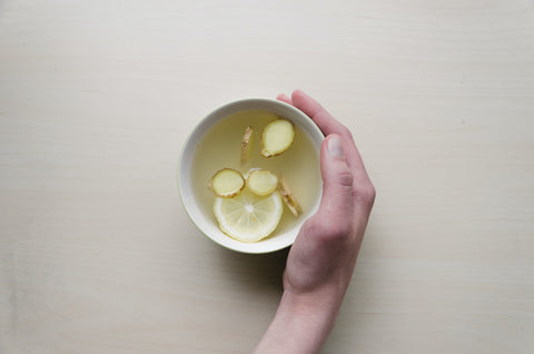 A hand holding a cup of tea with lemon and ginger.