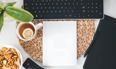 A cup of tea with lemon and a blank notepad in front of a computer keyboard.