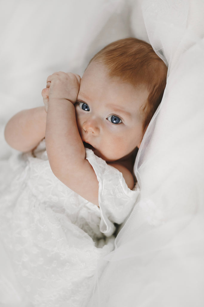 Baby girl is lying white blanket with big clear blue eyes