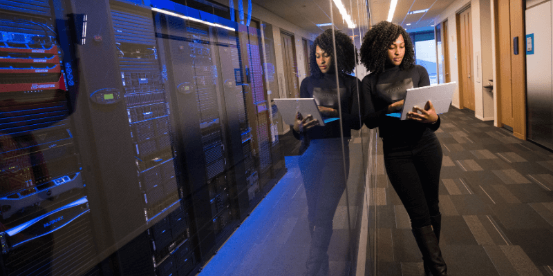 woman in black top using silver laptop near cabinets in data storage center