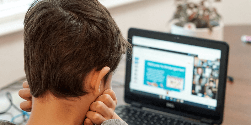 Kindergarten boy in gray shirt using black laptop for virtual learning