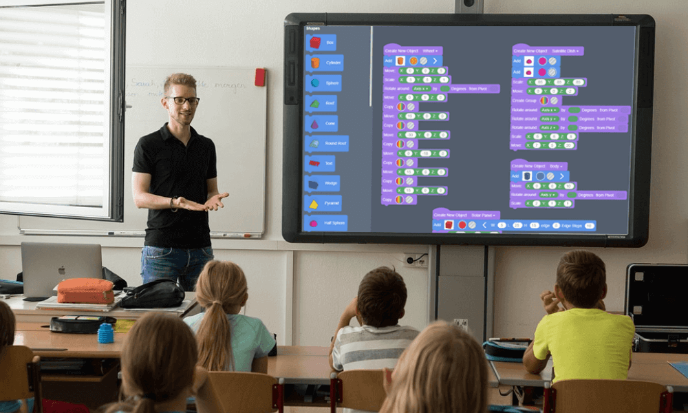 Image of a male teacher standing in front of classroom with a block-based coding program on the screen