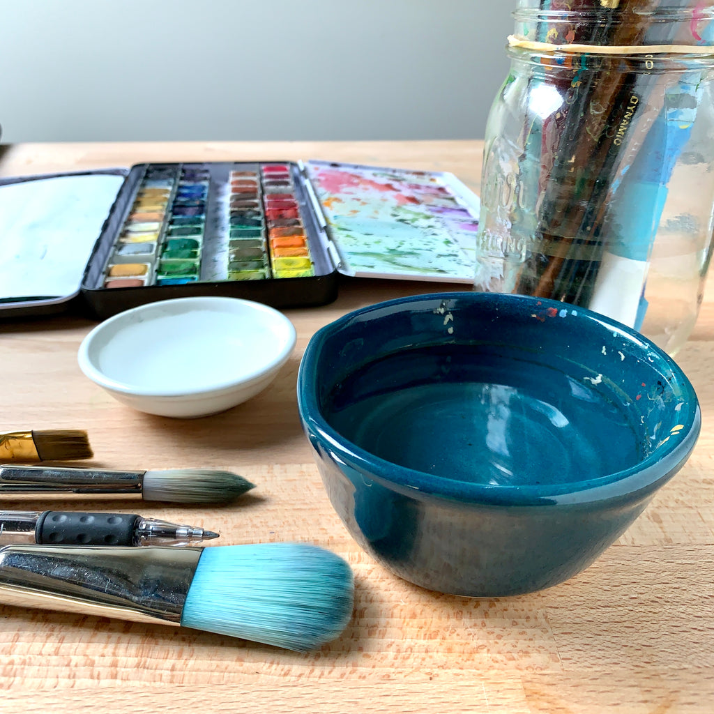 Close up image of 2 bowls of water and some brushes on a wooden table
