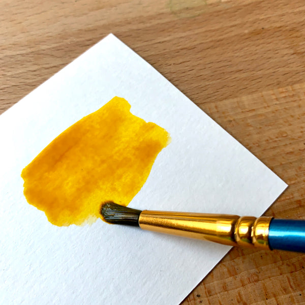 Close up of a yellow orange paint being painted via brush on watercolour paper