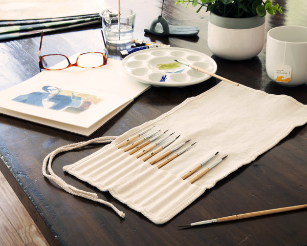 messy desk with art supplies like paint brushes, art palettes and paints