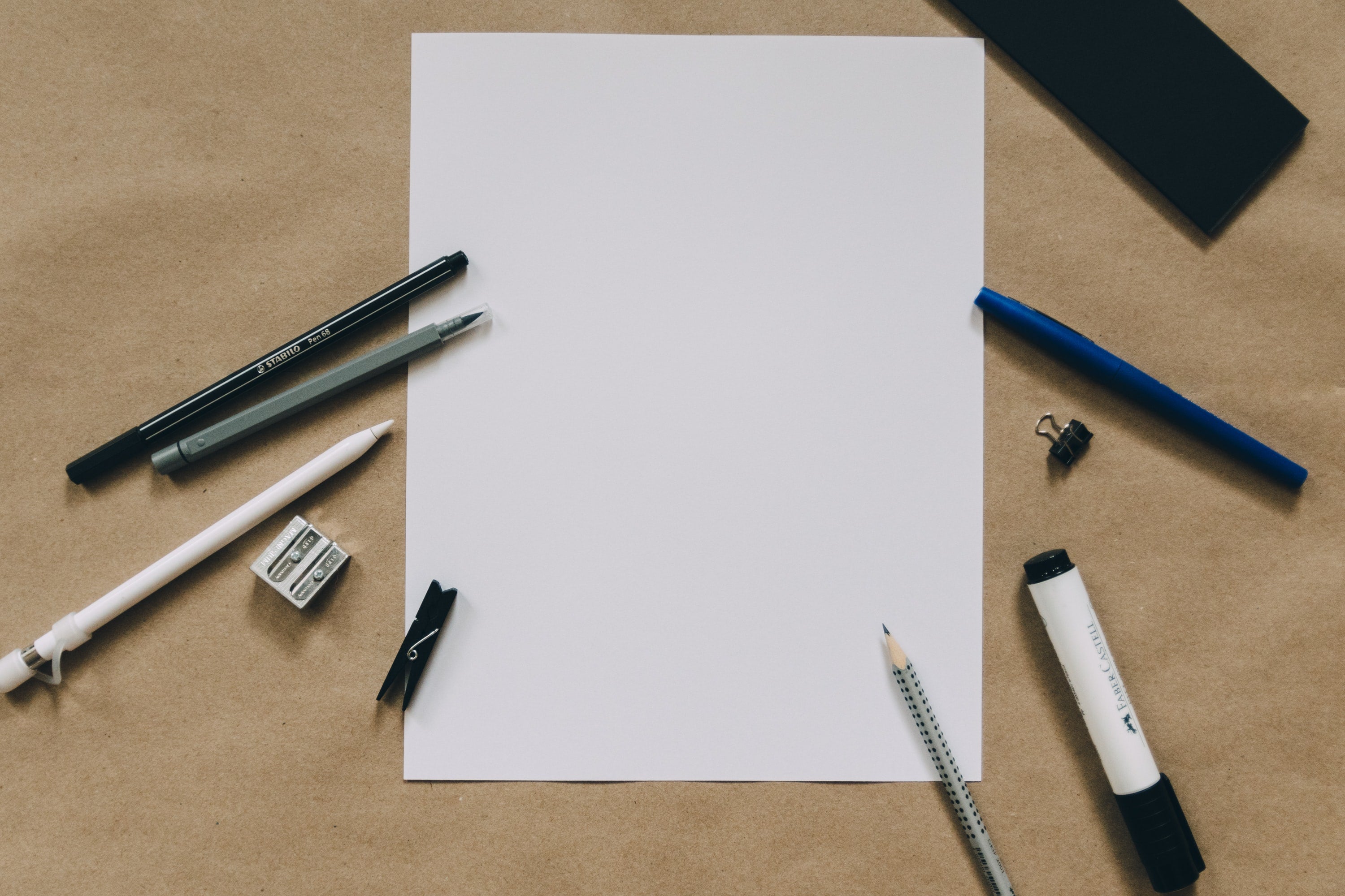 Birds Eye View of blank piece of paper with various types of pens around it - photo by Kelly Sikkema
