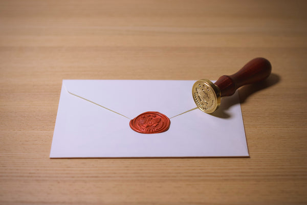 Image of a white envelope with a red wax seal and stamp off to the side 