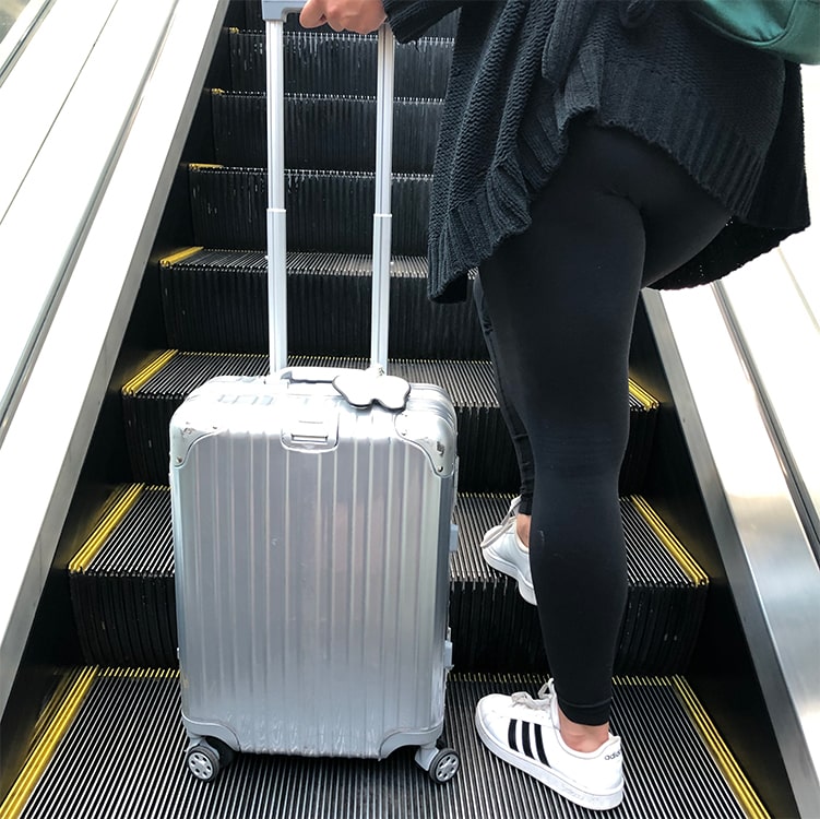 Woman on escalator with silver suitcase and tooth tag 