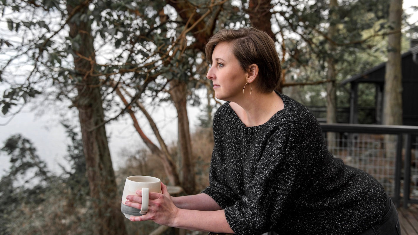 Picture of me holding a Large Sunset Mug on a deck with pine trees and Penn Cove in the background.