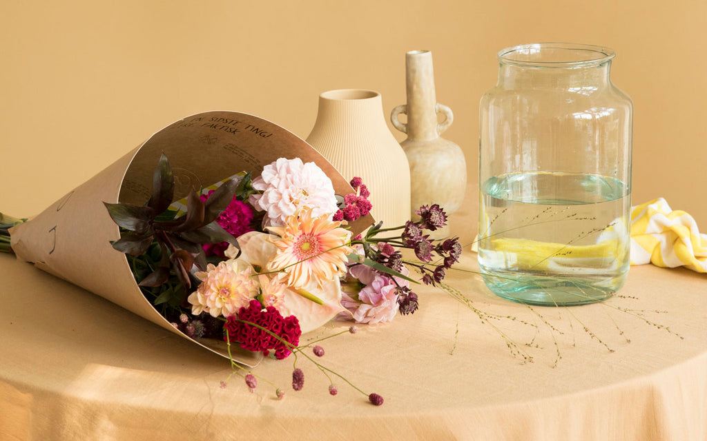 Bloomon Bouquet in Pappverpackung auf einem Tisch mit einem Krug Wasser