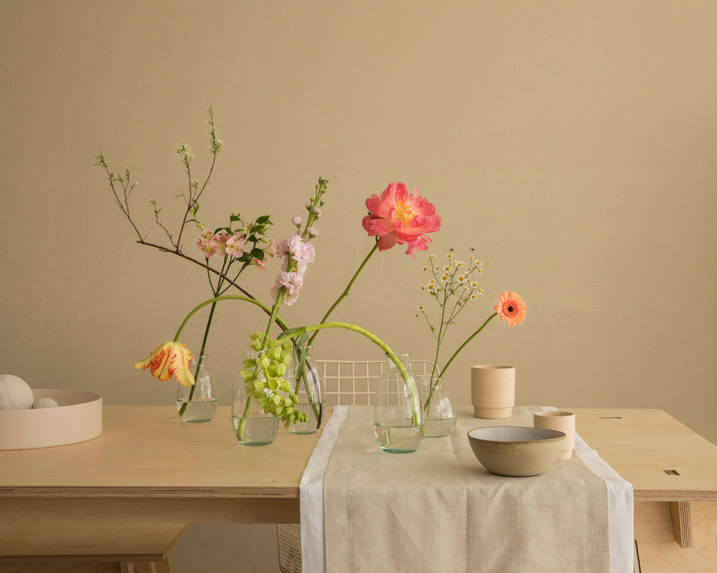 Blumen in blühenden Mini-Glasvasen auf einem gedeckten Tisch