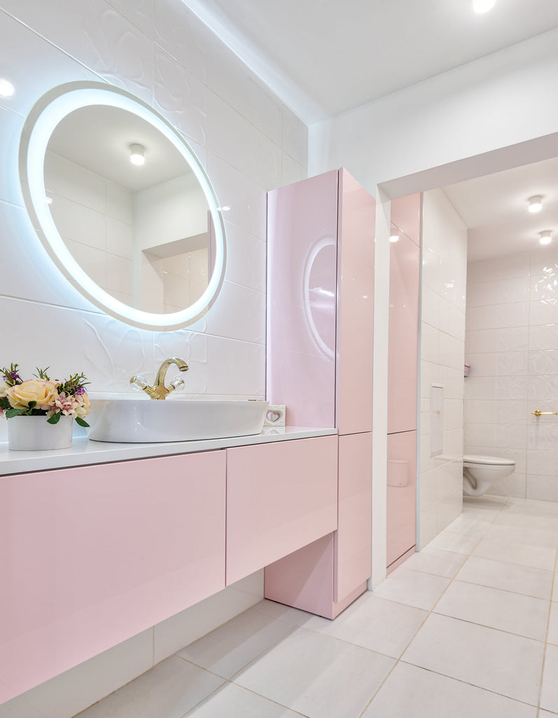 a coral pink bathroom with a floating, backlit circular mirror