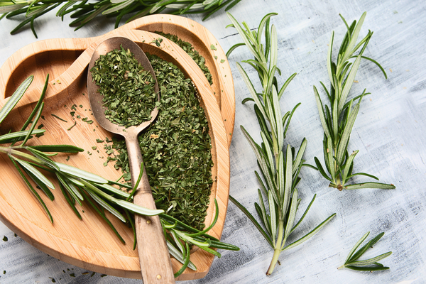 Image of fresh herbs - basil, parsley, thyme, rosemary, and cilantro - arranged in a row on a wooden cutting board, with a knife next to them.
