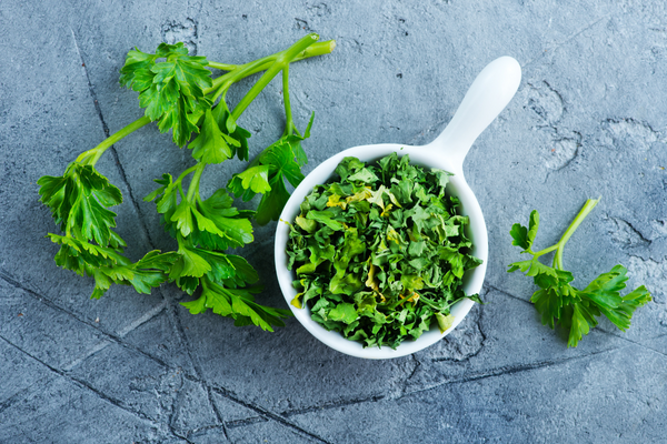 Image of fresh herbs - basil, parsley, thyme, rosemary, and cilantro - arranged in a row on a wooden cutting board, with a knife next to them.