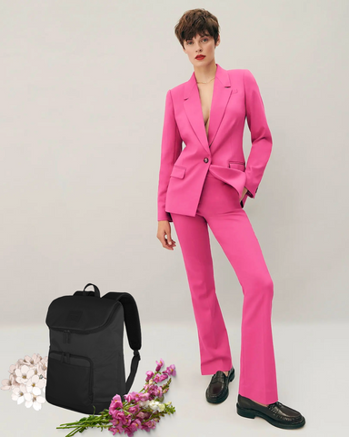 Tribeca Backpack with fresh pink flower next to model with pixie cut & hand in hot pink power suit pocket, looking ready for business