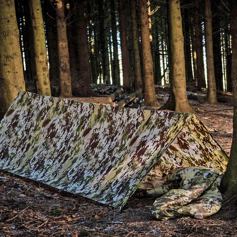 Lightweight camouflage print tarp set up as a tent between trees  