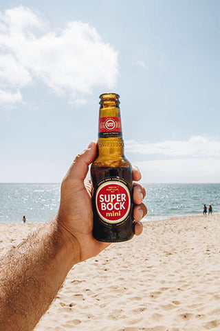 homem segurando uma cerveja bock na praia