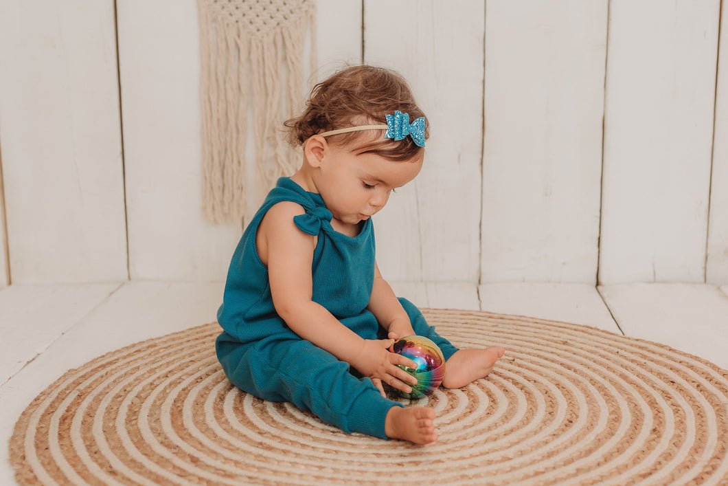 baby girl sits on the bohemian mat playing with a metal ball whilst wearing her handmade teal blue lounge comfy romper adjustable straps cosy winter clothing