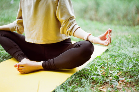 woman sitting down meditating to relax outside on yoga mat in backyard