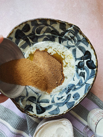 Top view of blue patterned bowl with wet ingredients in it. There's a second smaller bowl to the left with flour and other dry ingredients in it being poured into the wet ingredient mix.