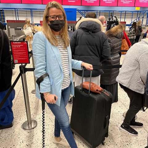 Blonde woman wearing a mask with her suitcase and crutches travelling in an airport