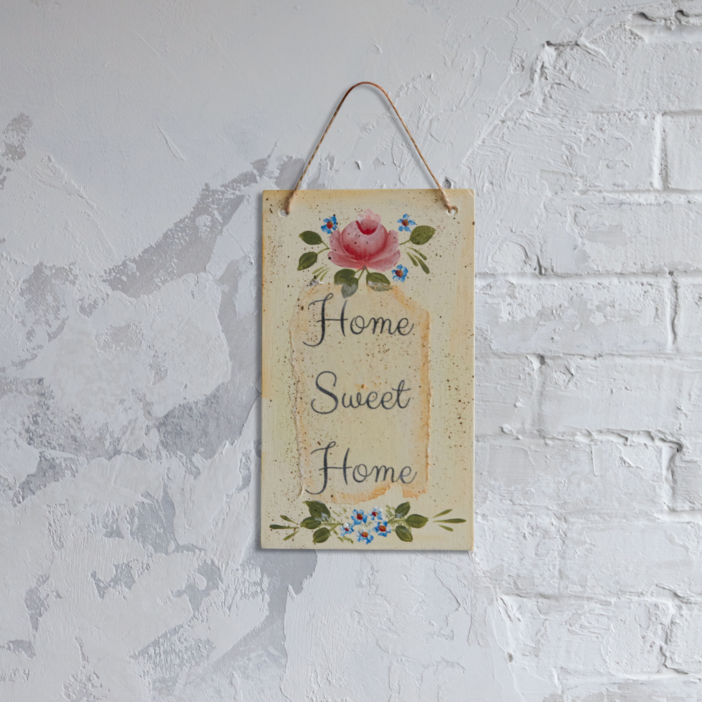 Painted wooden plaque decorated with roses and other flowers featuring text that reads “Home Sweet Home” against a brick and concrete background