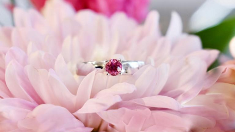 bague en or blanc avec une tourmaline rose posée sur une fleur rose pâle