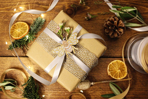 A gift is wrapped brown paper and silver ribbon with a silver and gold embroidered bee motif on top.