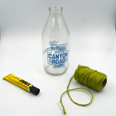 A milk bottle, a tube of UHU glue and a reel of green jute twine are placed on a white backdrop