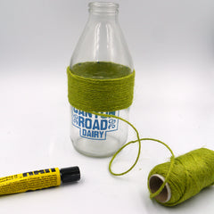 A tube of UHU glue lays on the table next to a milk bottle which has been half wrapped in green twine