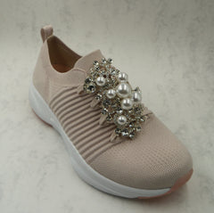 A large brooch is pinned to the front of the trainers. The brooch has large pearls and diamante jewels on it.