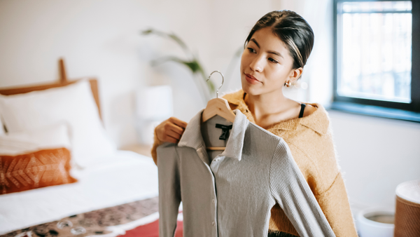 a woman looks at herself in the mirror holding a shirt in front of her