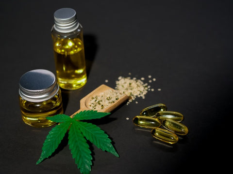 Cannabis leaf on a black background. With glass bottles of oil the left of it and raw material on the right. Symbolizing the various forms CBD can take once processed. Such as an isolate in Tres Keikis Natural Relief lotion with CBD