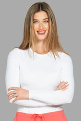 A young female LPN wearing a white underscrub and coral scrub pant on a grey background.